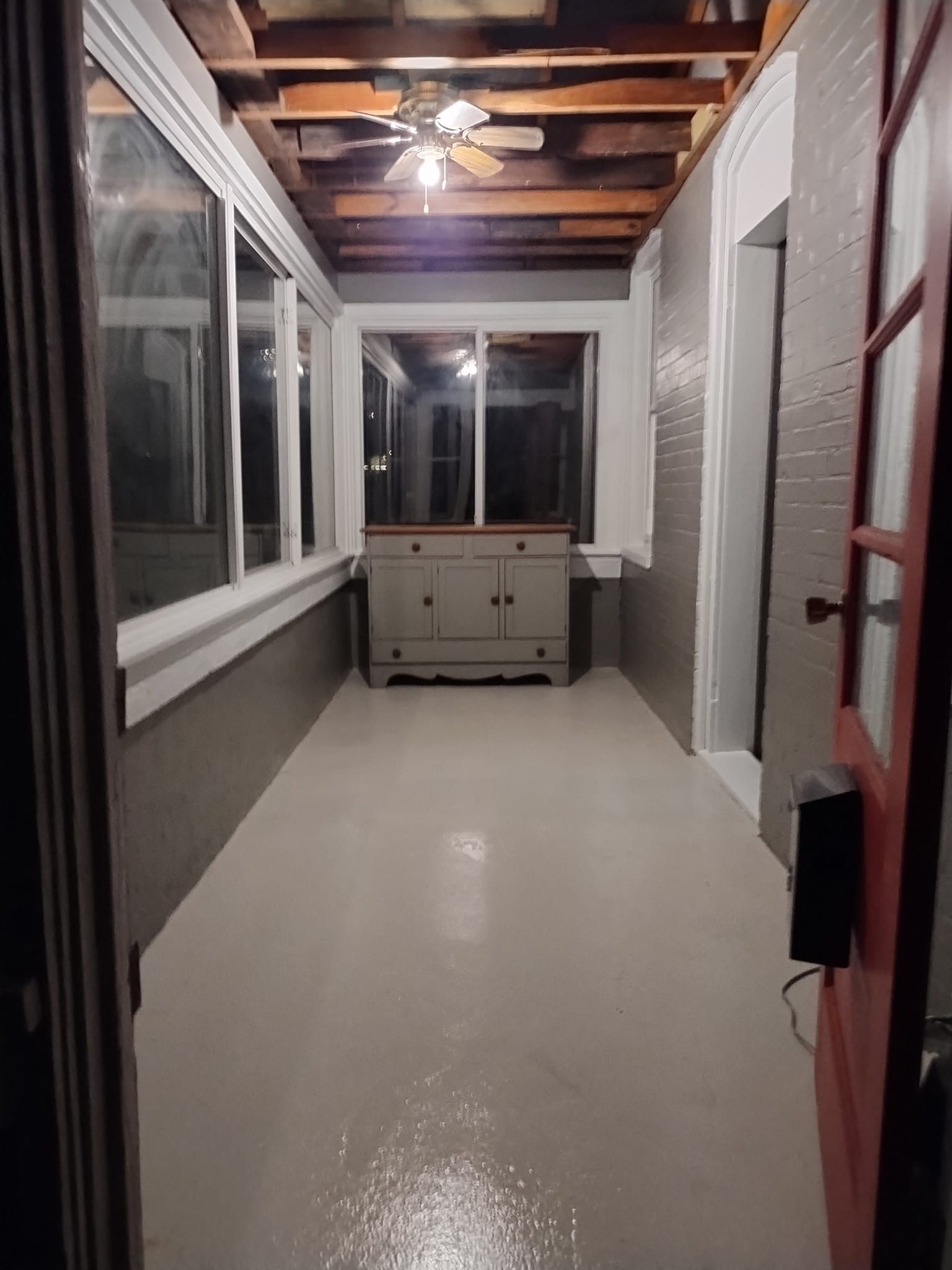 Interior of a sunroom with gray walls, light floor, and a cabinet. Windows line the left wall. Open door on the right.