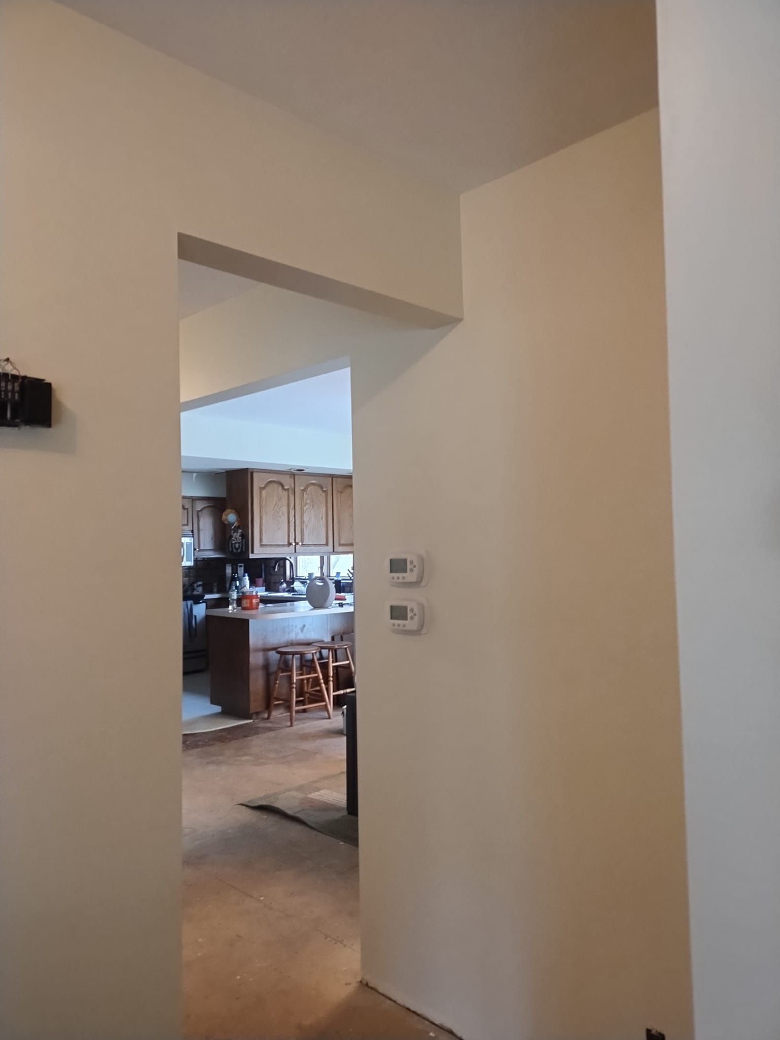 Hallway opening into a kitchen. Beige walls with an opening framed by a header. Thermostats are on the right wall.
