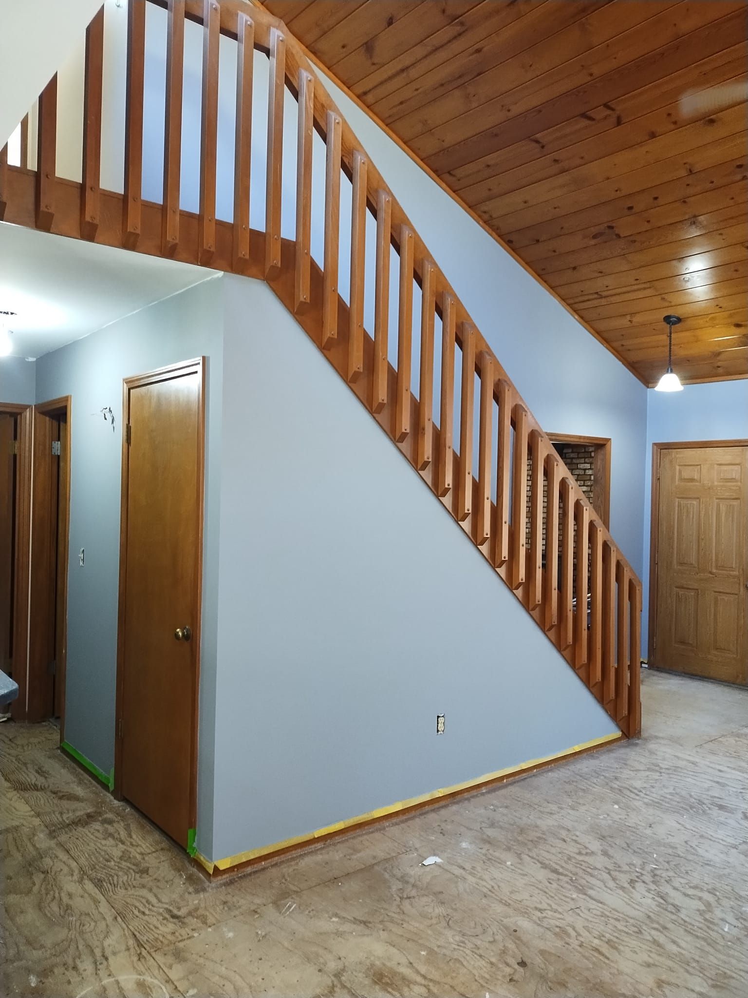 Interior view with wooden staircase, blue walls, wood doors, and brown flooring.