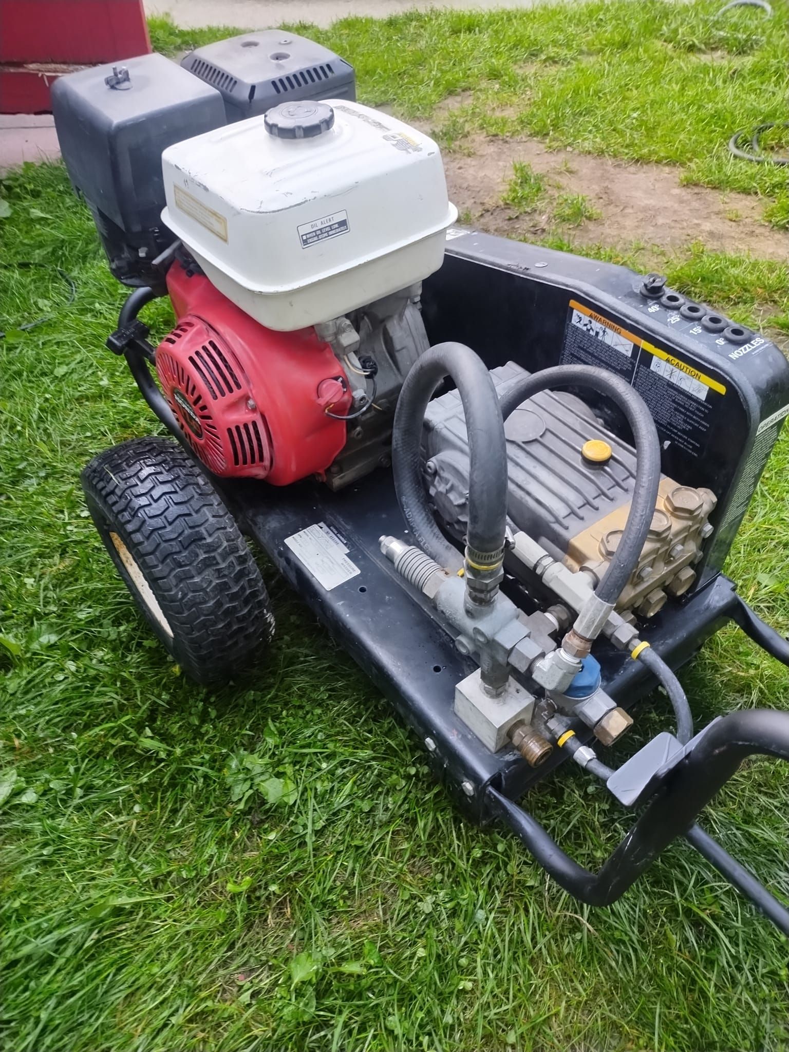 Gas-powered pressure washer on a grassy lawn, featuring a red engine and black frame.