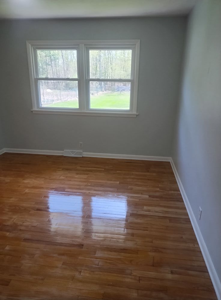 Empty room with hardwood floors, two windows, and gray walls.