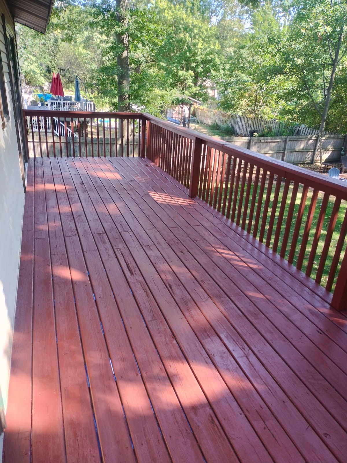 Wooden deck painted red with railing, set in a backyard with trees.