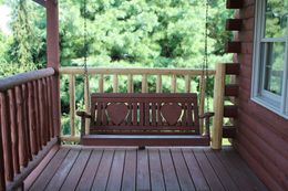 Wooden porch swing with heart cutouts, overlooking a lush green forest.