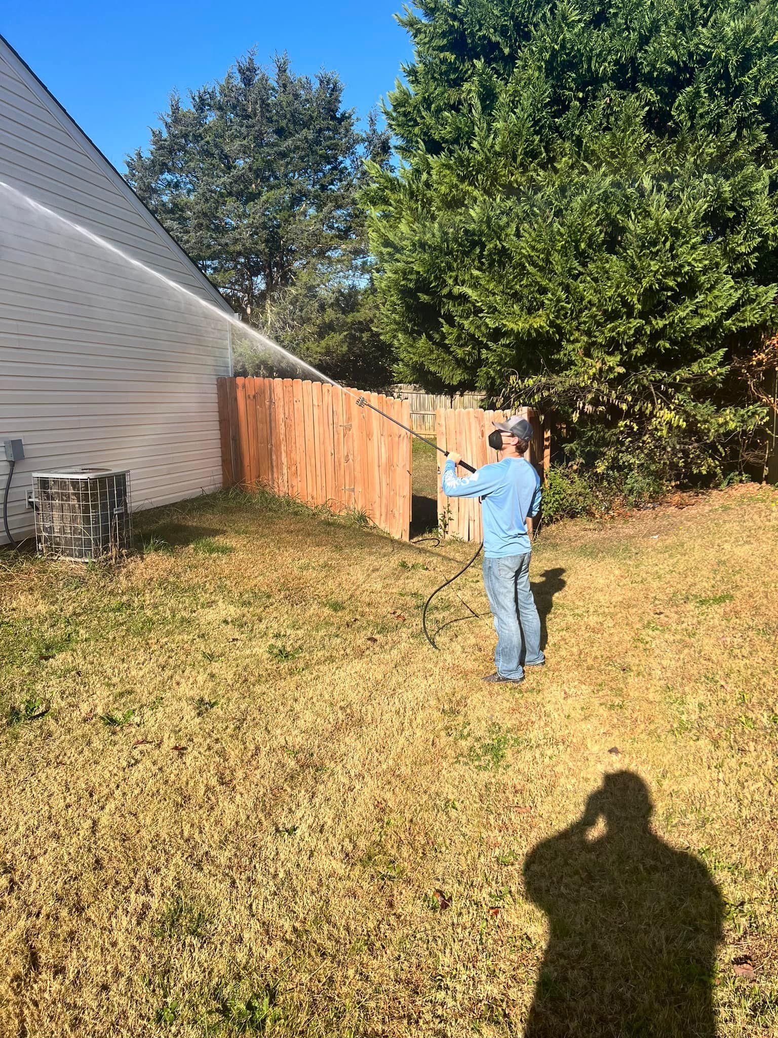 Person taking a photo of a wooden fence in a backyard on a sunny day.