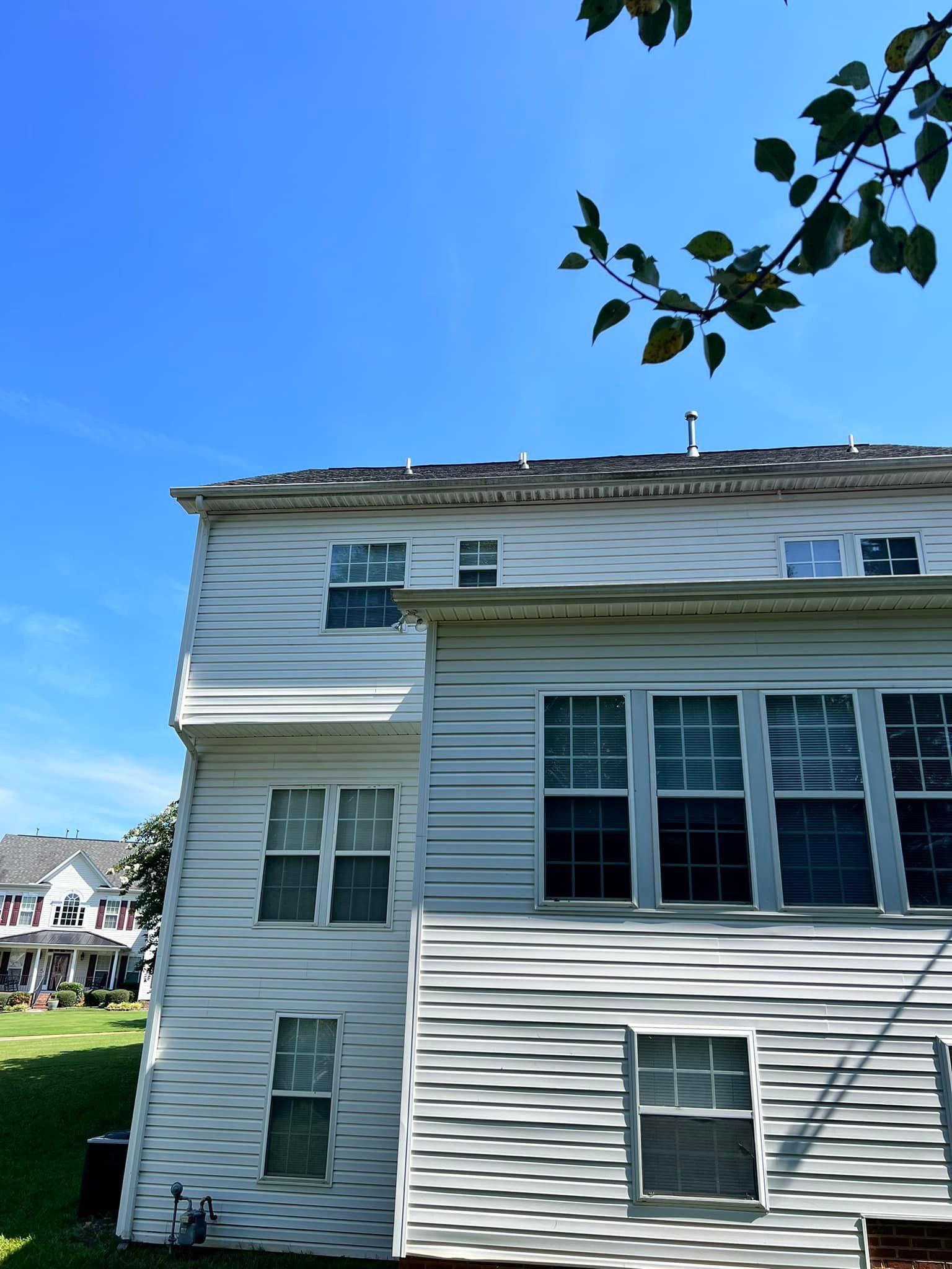 White two-story house against a blue sky, with visible windows, siding, and a tree branch in the top right.