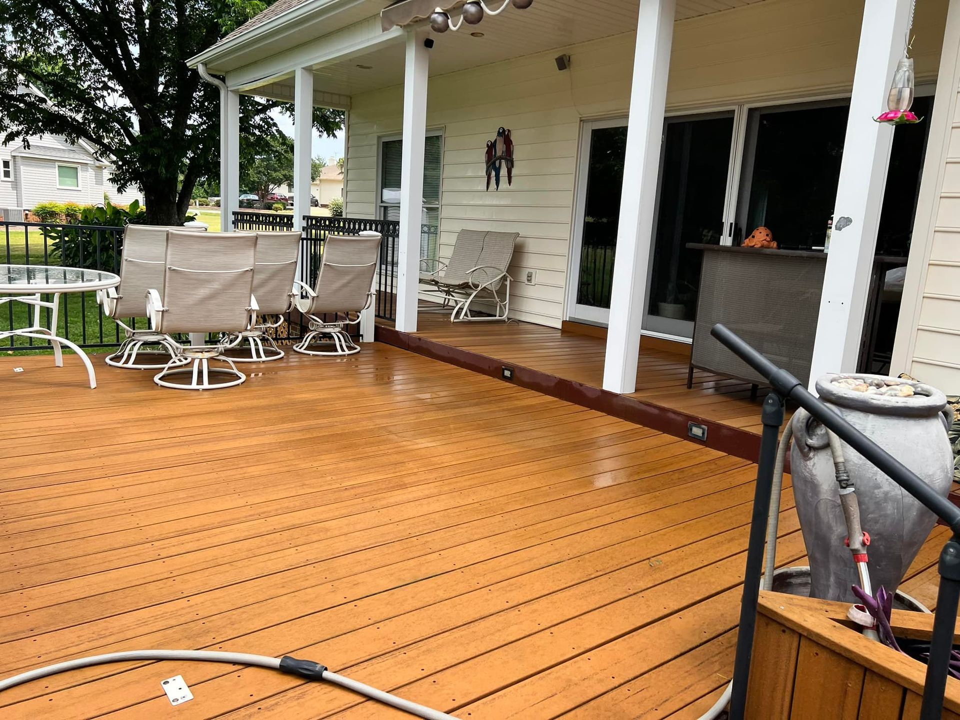 Wooden deck with tan chairs and table, attached to a light yellow house with a covered porch.