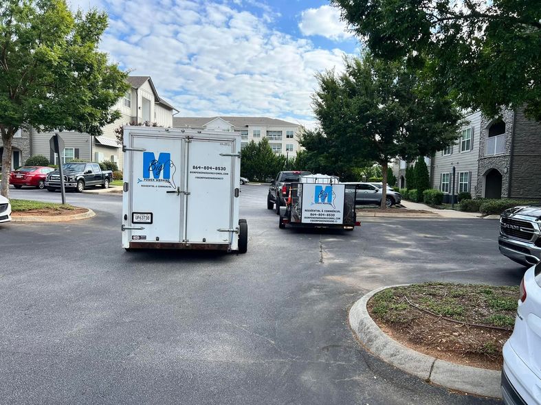 Two white trailers with company logos parked in an apartment complex parking lot.