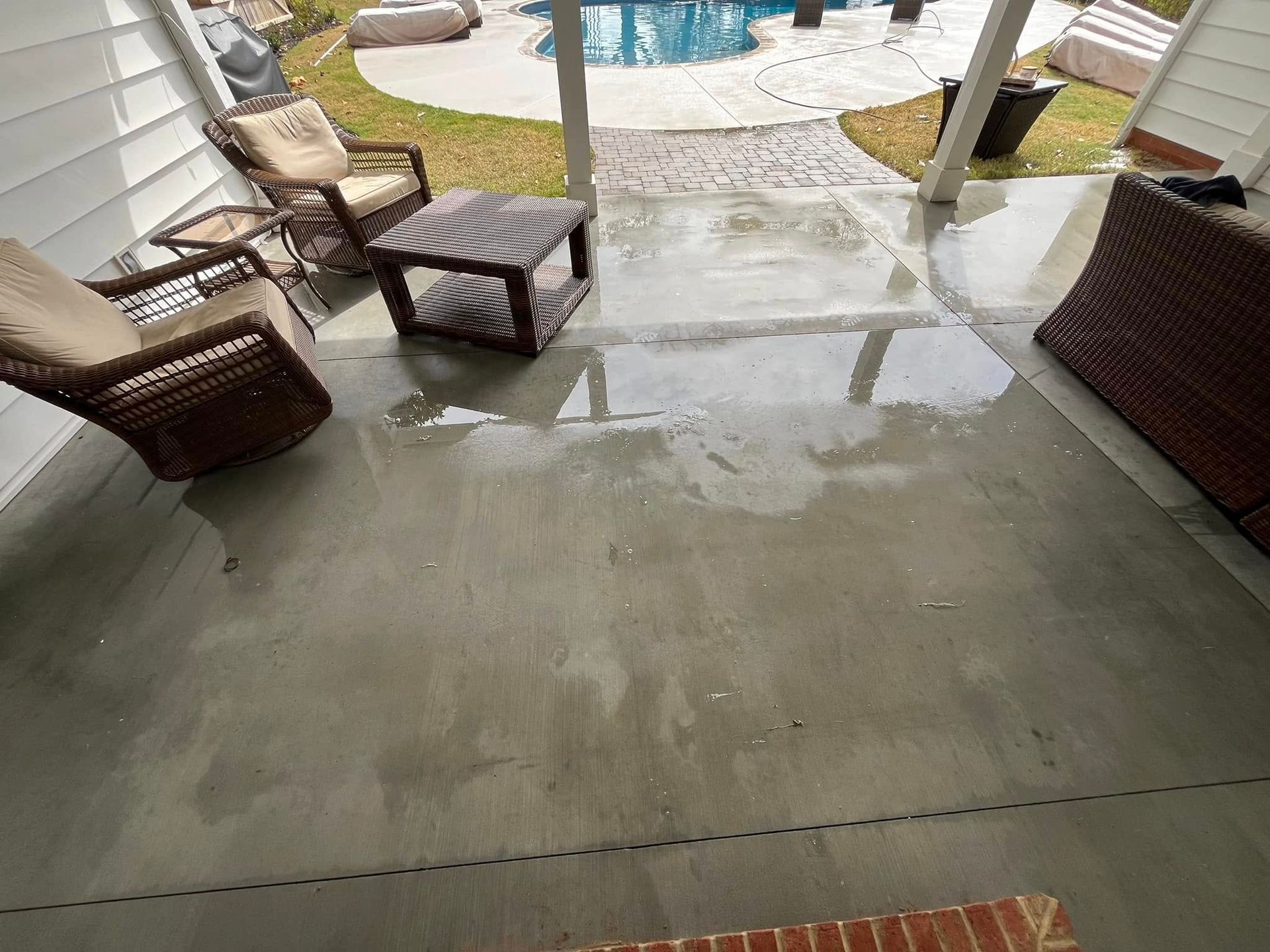Patio with wet concrete floor, outdoor furniture, and a swimming pool in the background.