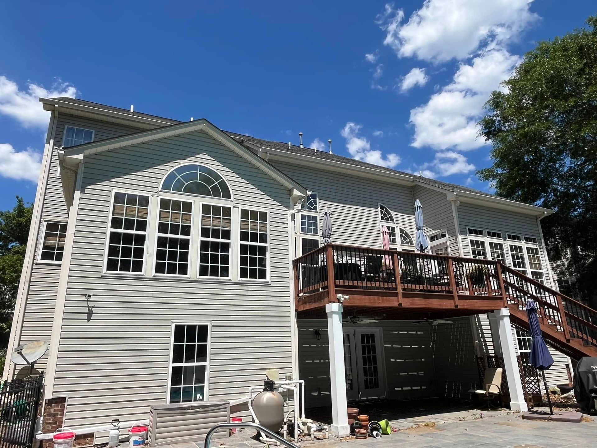 Back view of a light blue and white house with a wooden deck, blue sky with clouds.
