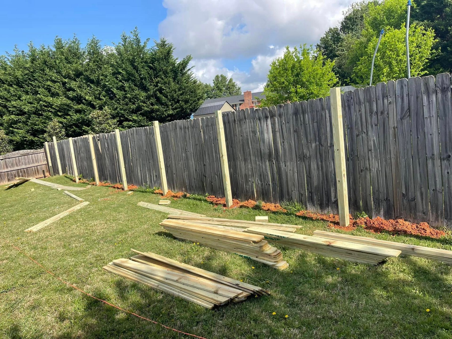 A weathered wooden fence in a yard, with new wooden posts and boards for repair or replacement.
