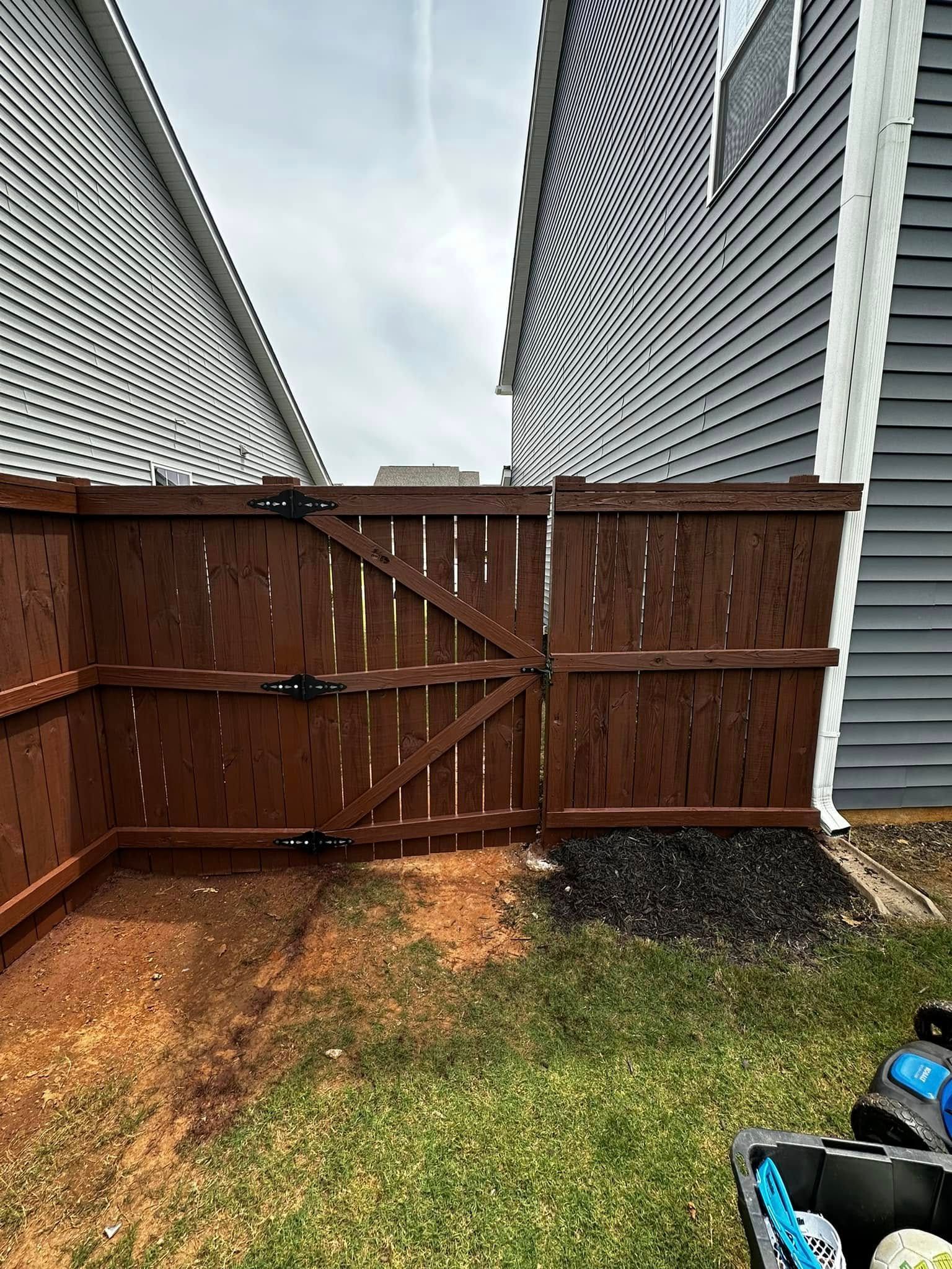Brown wooden fence between two houses, grassy yard in front.