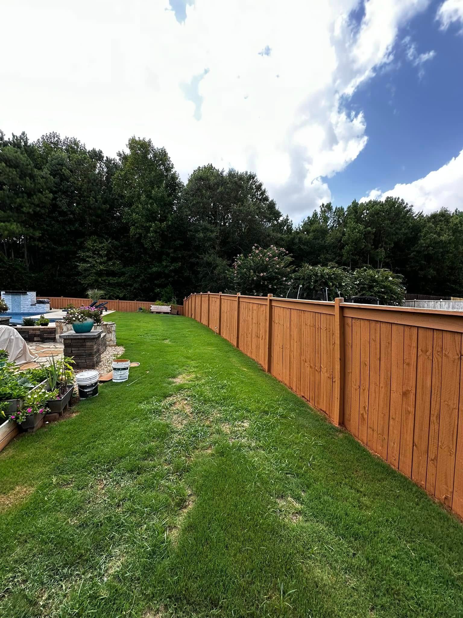 Green grass yard next to a wooden fence with trees and cloudy sky in the background.