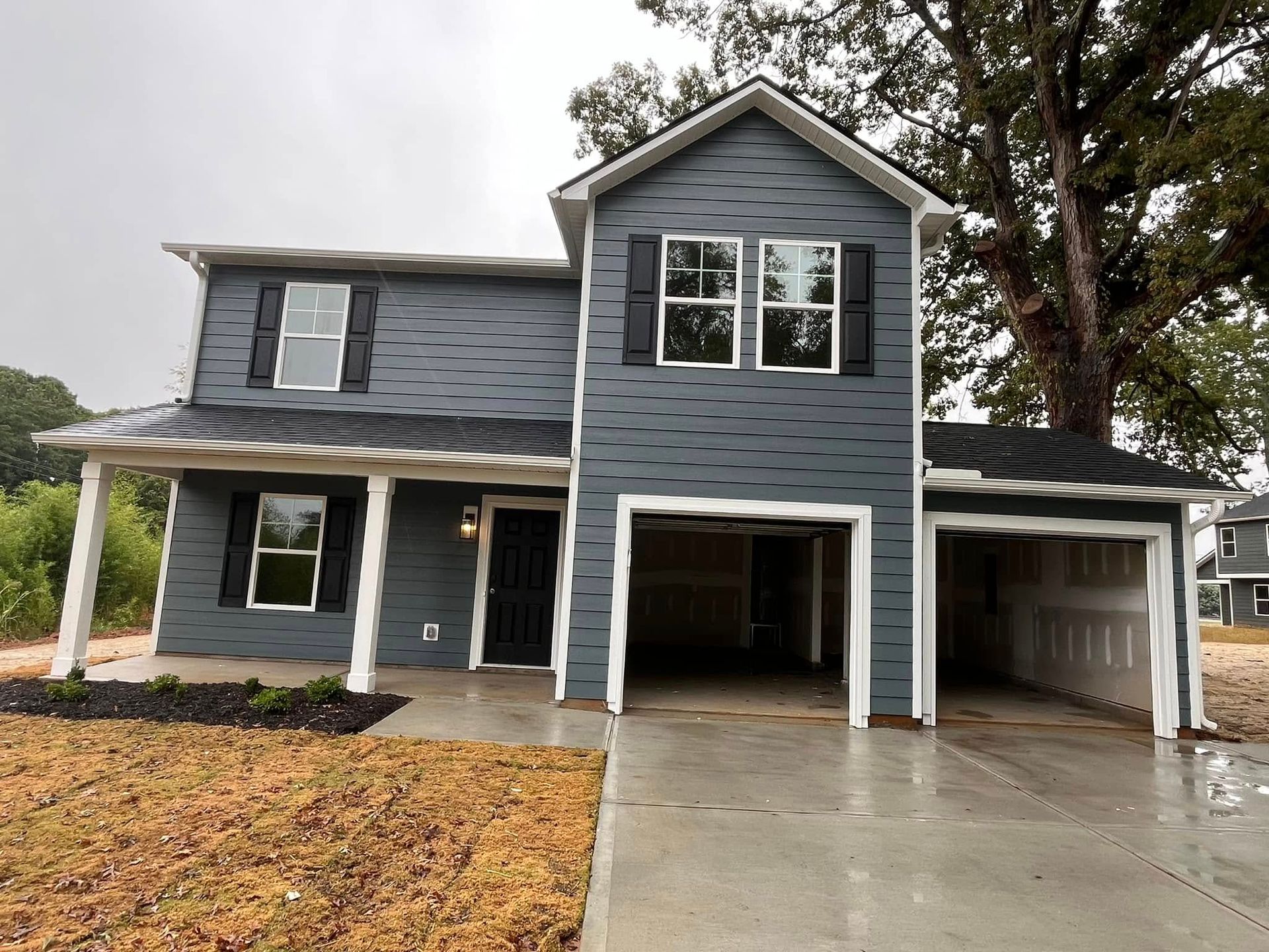 Two-story house with gray siding, open garage, and black shutters, on a rainy day.
