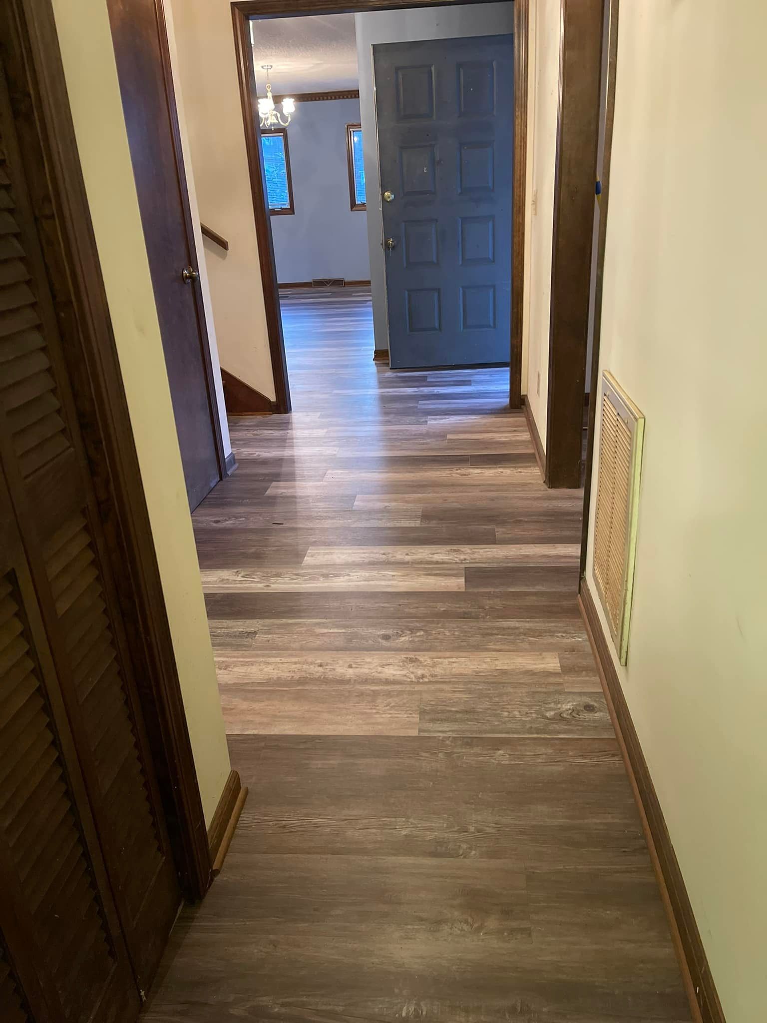 Hallway with wood-look flooring, doors on either side, and a blue door at the end.