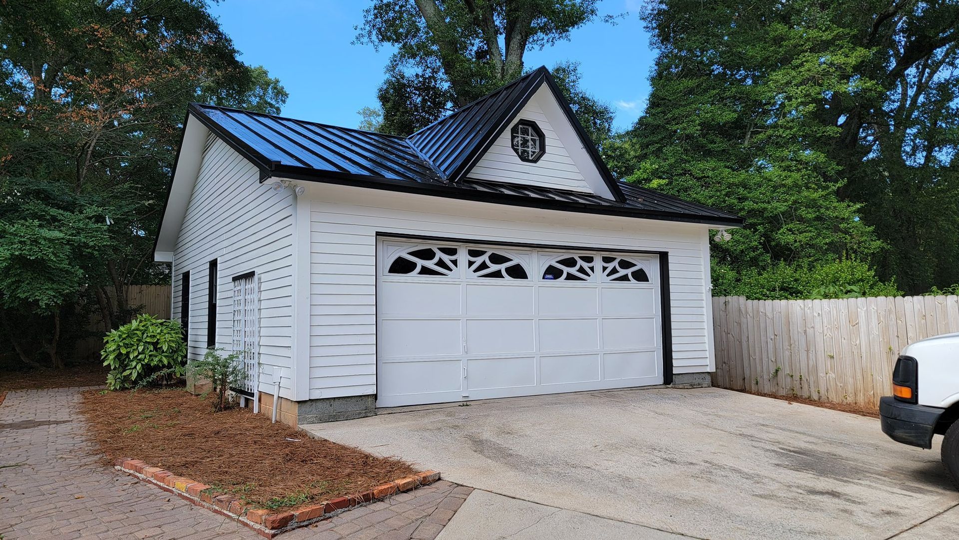 White garage with black roof and decorative window, fronting a gravel driveway.