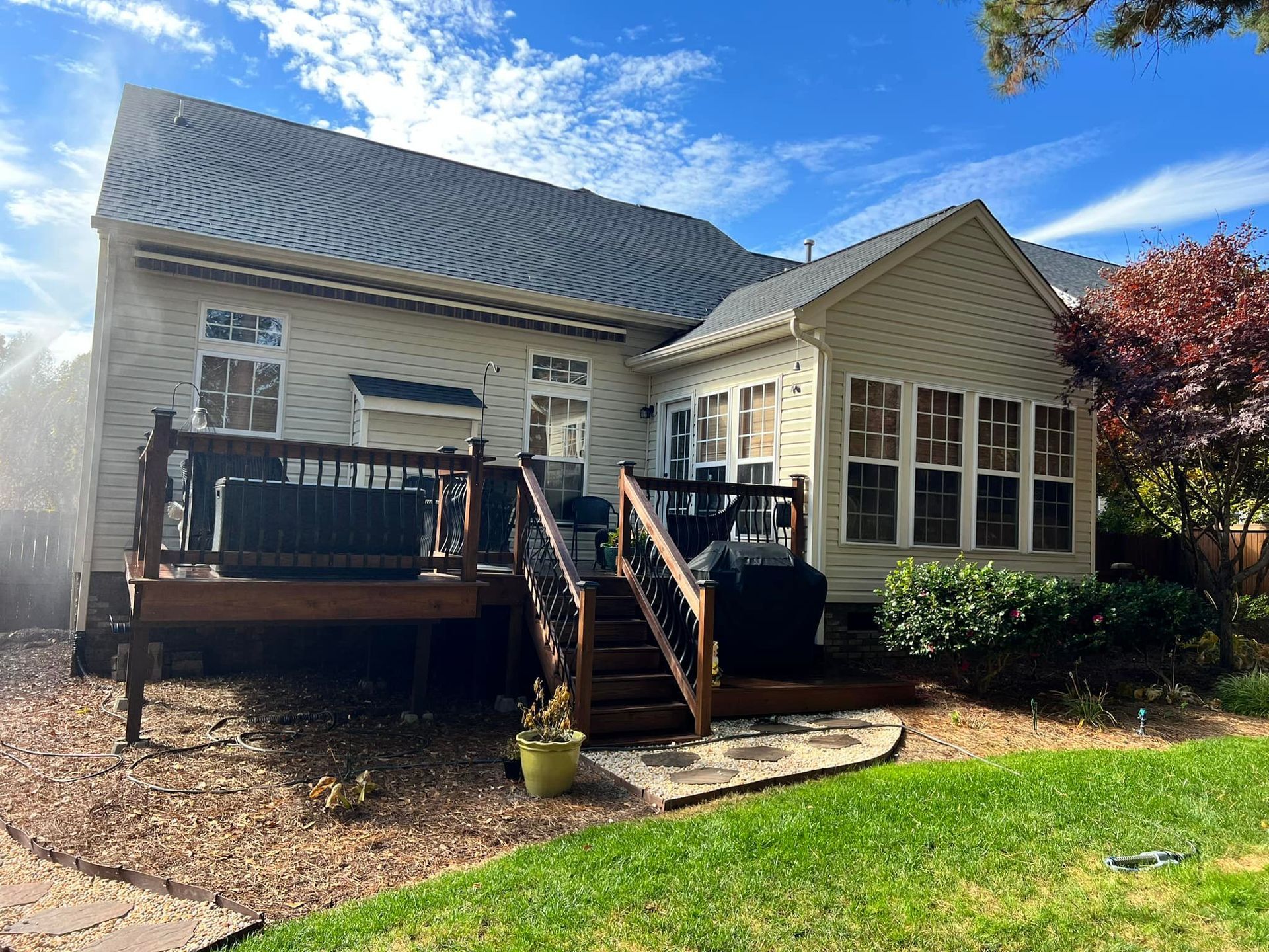 Backyard deck with stairs, beige house, green grass, blue sky, and trees.