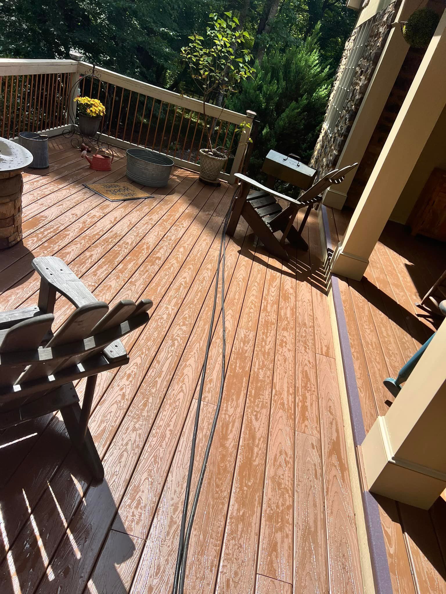 Wooden deck with two chairs, potted plants, and a light-colored railing in an outdoor setting.