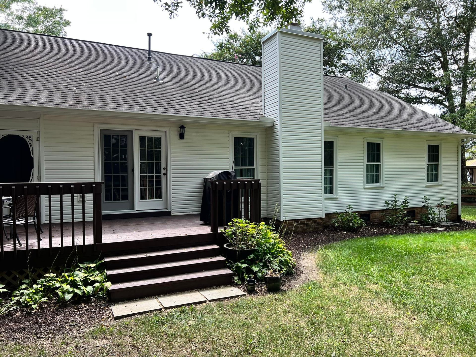 Back of a white house with a deck and chimney, set in a grassy yard.