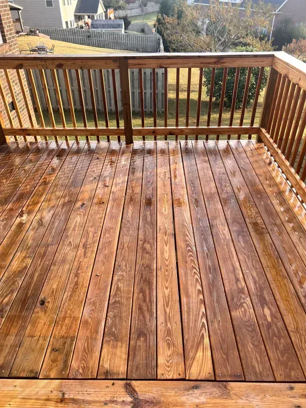 Wooden deck with railing, stained brown, overlooking a backyard.