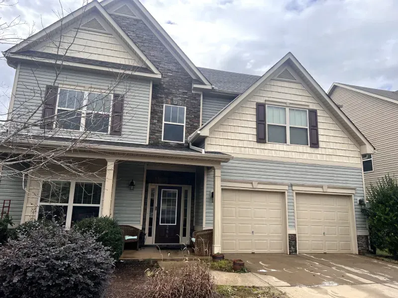Two-story house with blue siding, brown shutters, and a two-car garage under a cloudy sky.