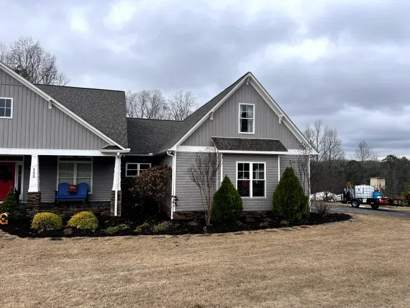 Gray house with dark roof, landscaping, and overcast sky.