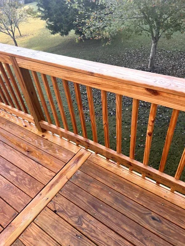 Wooden deck railing overlooking a grassy yard and trees.