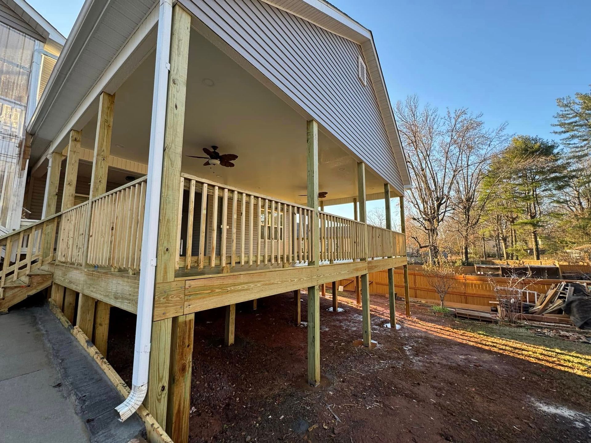 Wooden deck with railing and columns, beneath a building's overhang; outdoor setting.