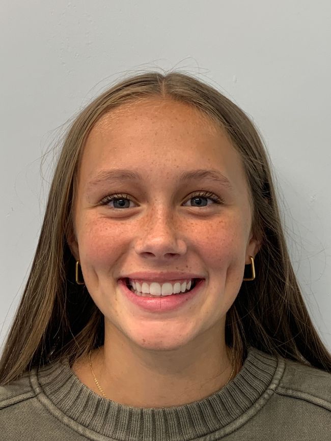 A young girl is smiling for the camera while wearing a sweater and earrings.