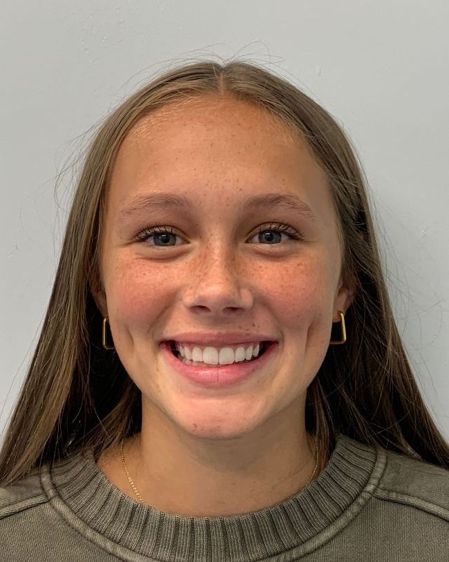 A young girl is smiling for the camera while wearing a sweater and earrings.