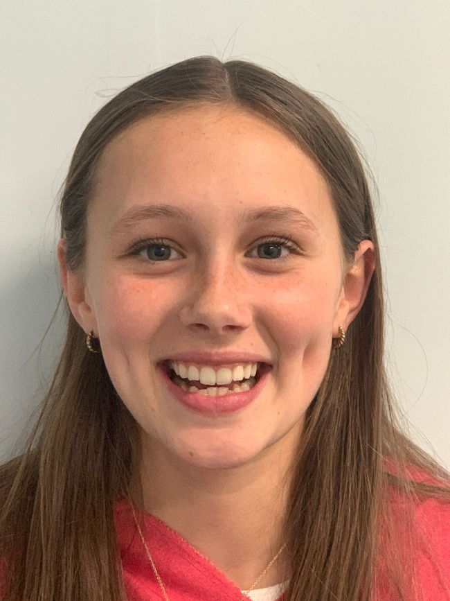 A young girl in a red shirt is smiling for the camera.