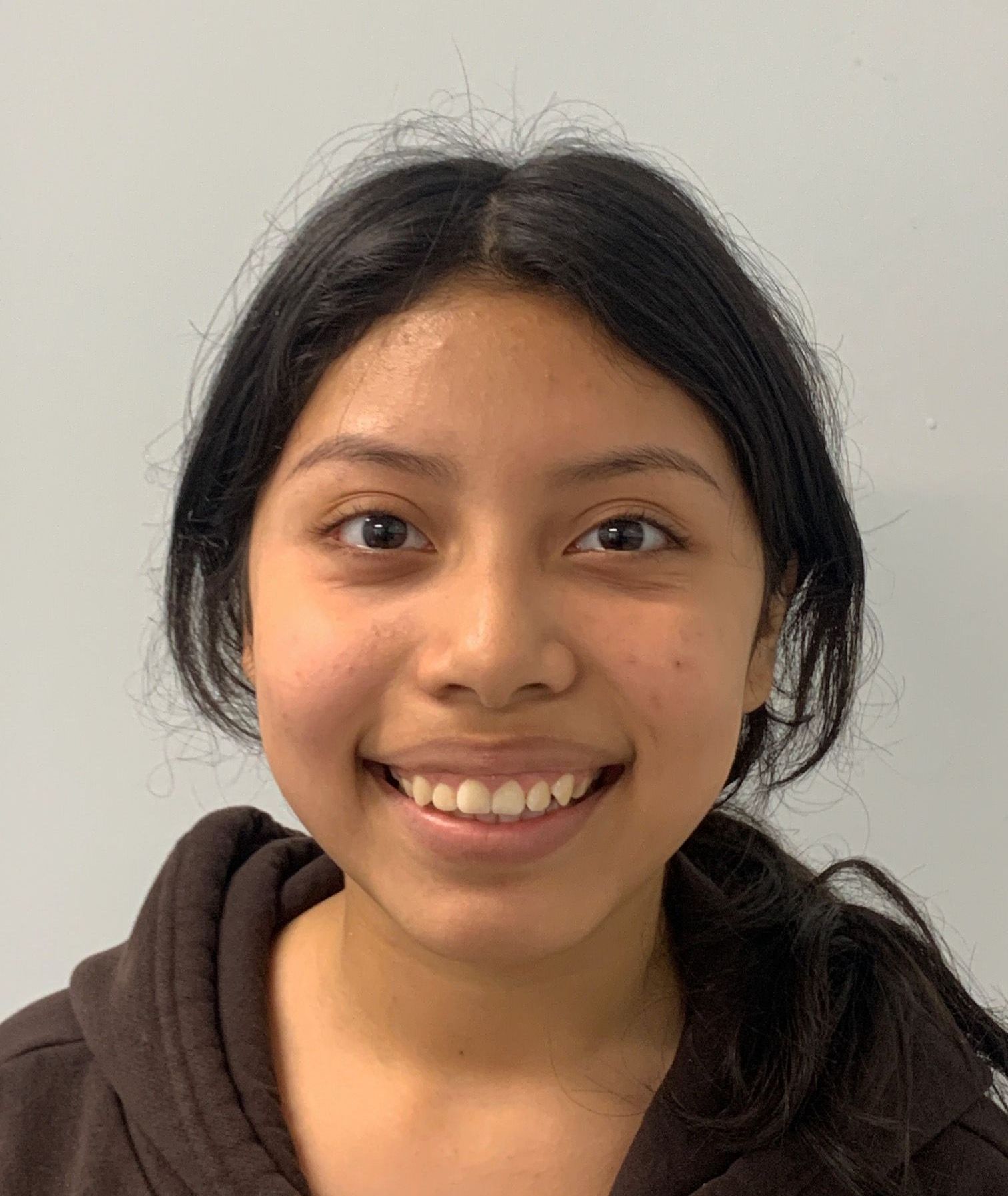 A young woman is smiling for the camera while wearing a brown hoodie.