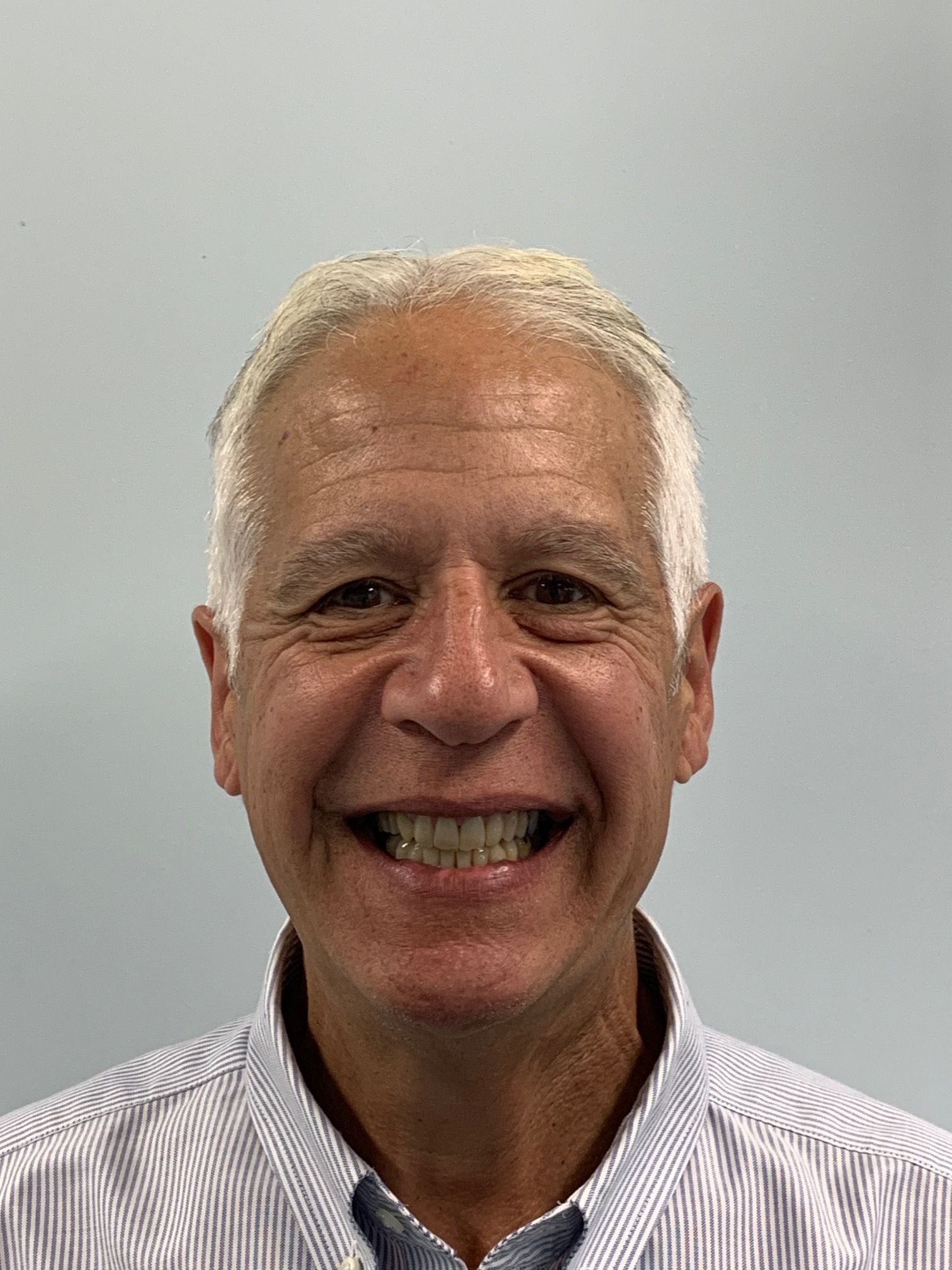 A man wearing a striped shirt and tie is smiling for the camera.