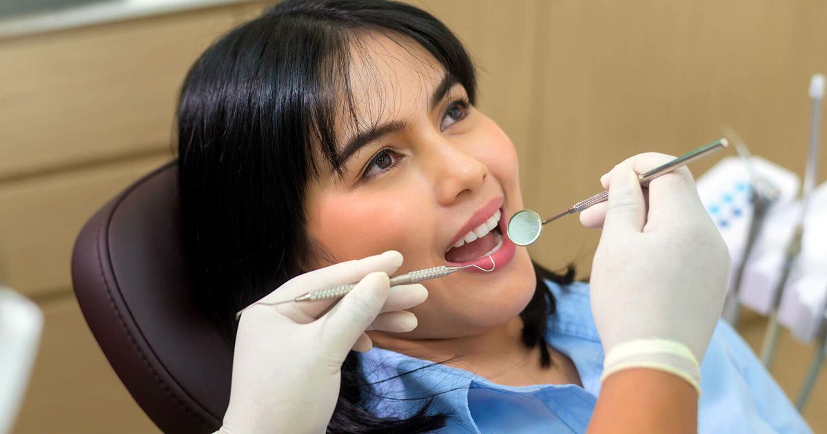 A woman is sitting in a dental chair getting her teeth examined by a dentist