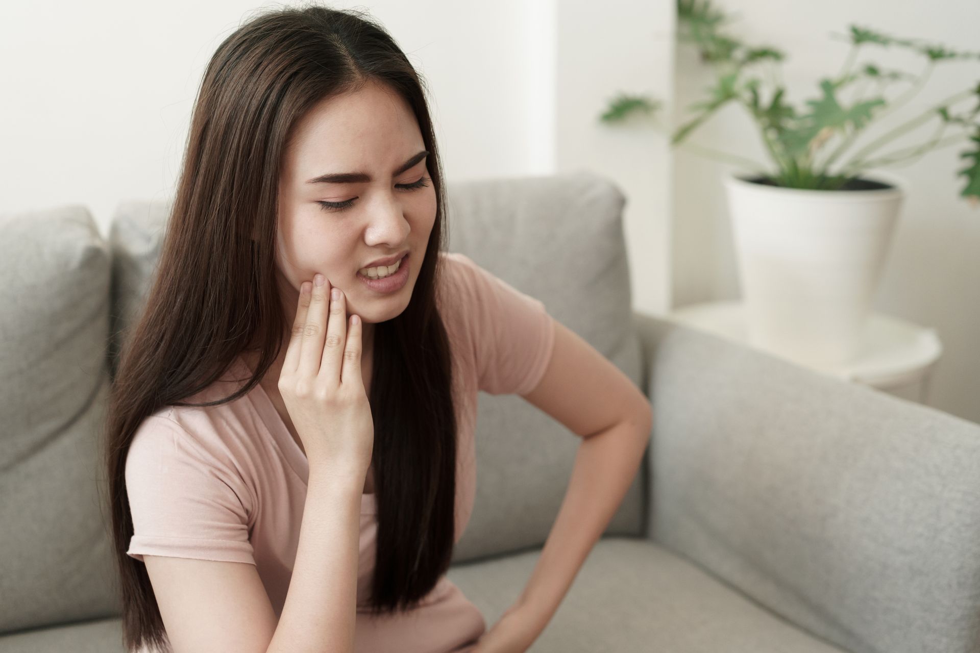 A woman is sitting on a couch with a toothache.