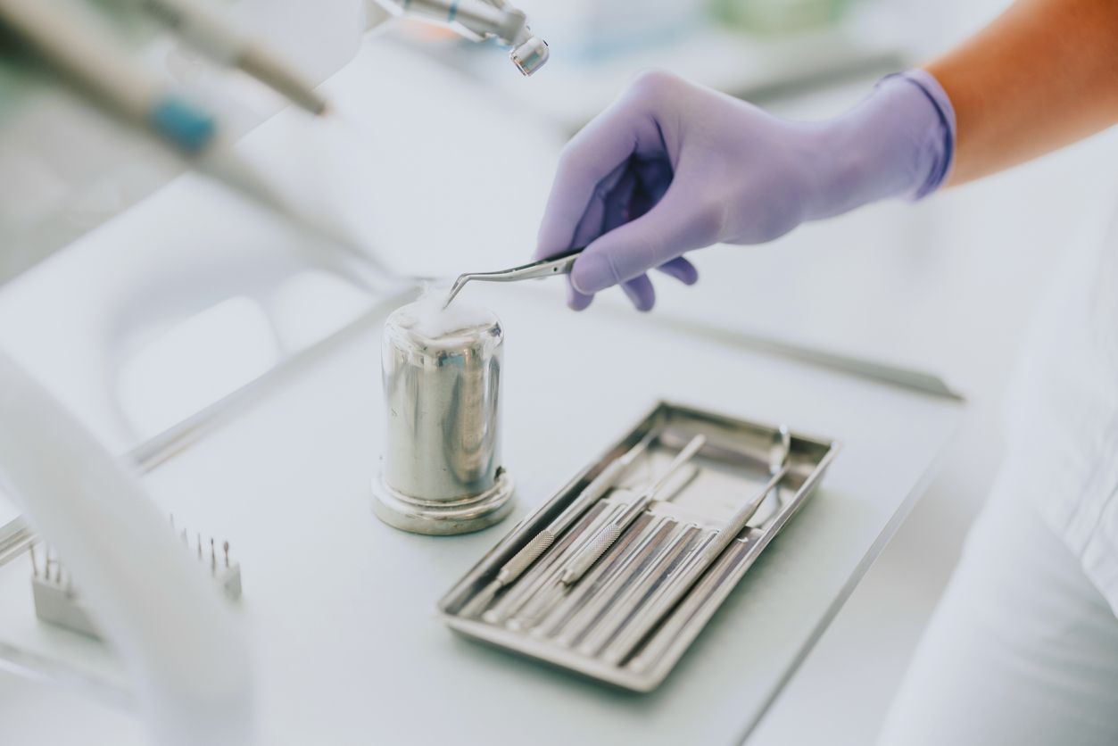 A dentist is holding a dental tool over a tray of dental instruments.