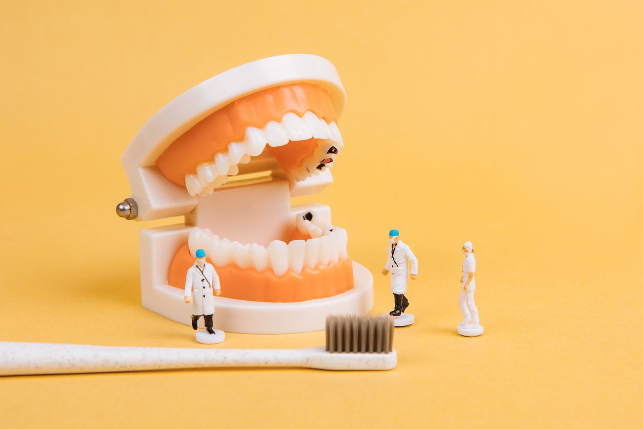 A toothbrush , a model of teeth , and miniature dentists on a yellow background.
