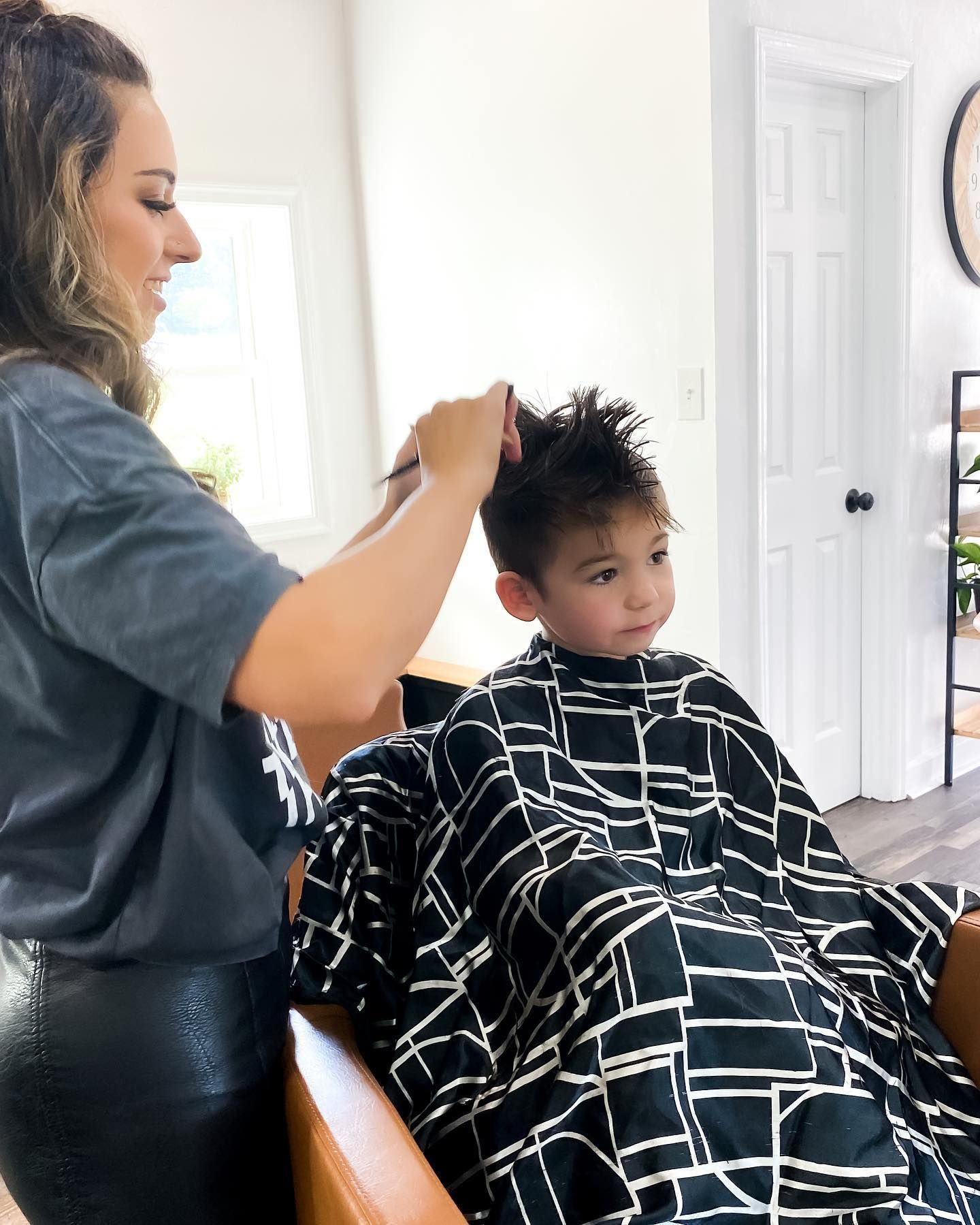 Woman cutting a child's hair in a salon; child wears a cape.