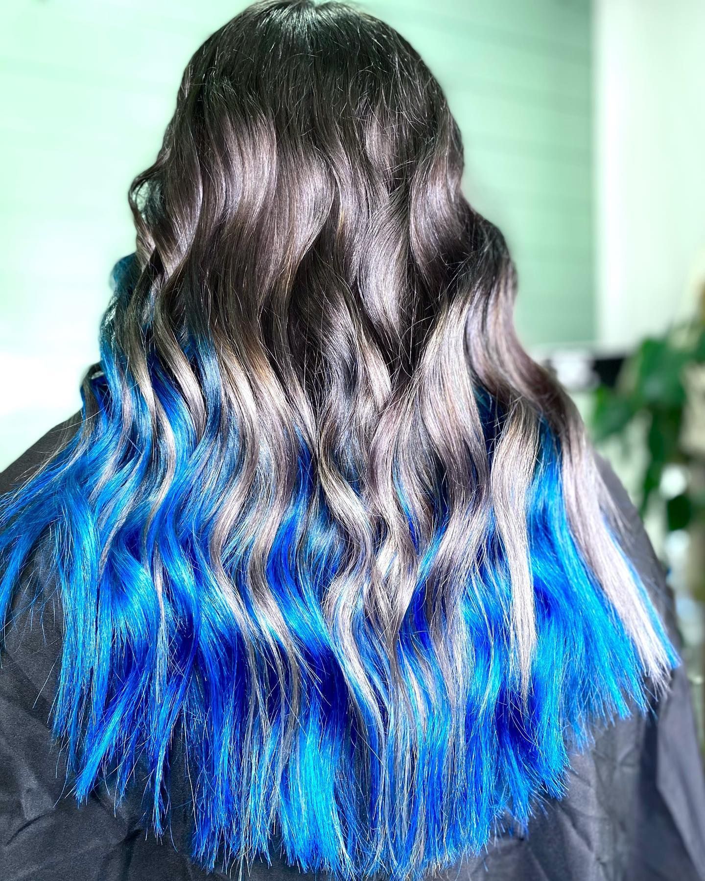Woman with dark hair, fading to blue tips. Wavy style, indoors.