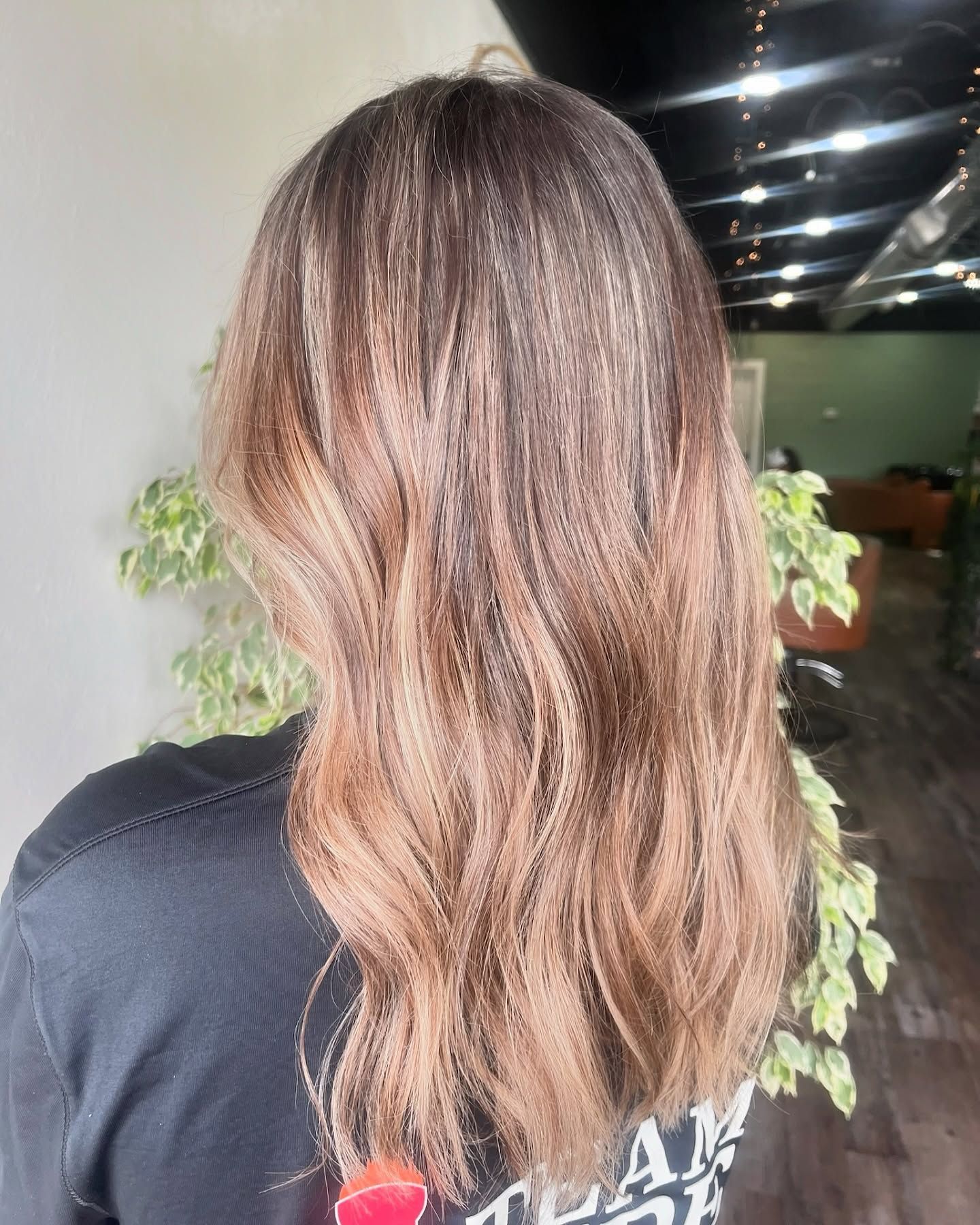 Woman's hair with dark roots transitioning to a light brown ombre, wavy style.  A black shirt is visible.
