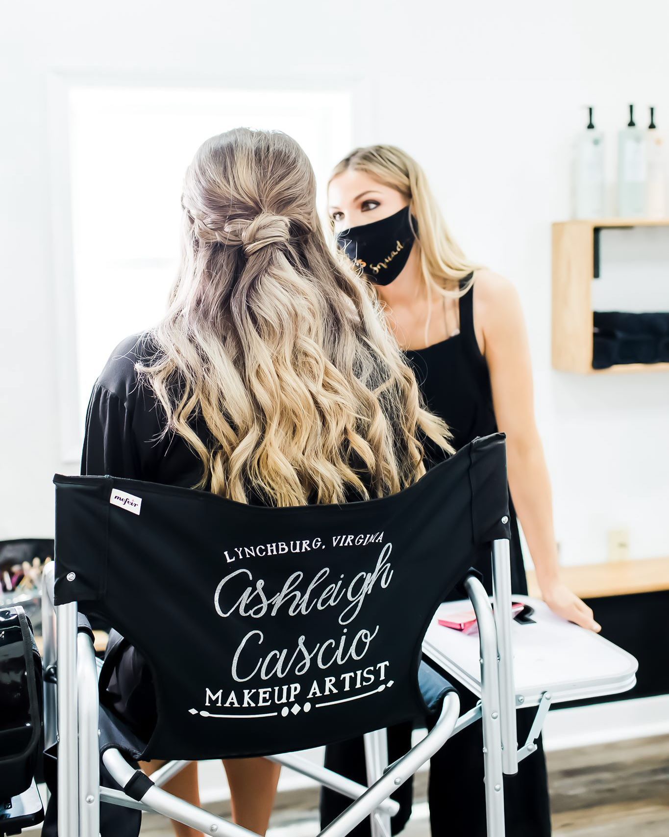 Makeup artist, Ashleigh Cascio, assisting a client. Makeup room. Client in chair, artist in mask.
