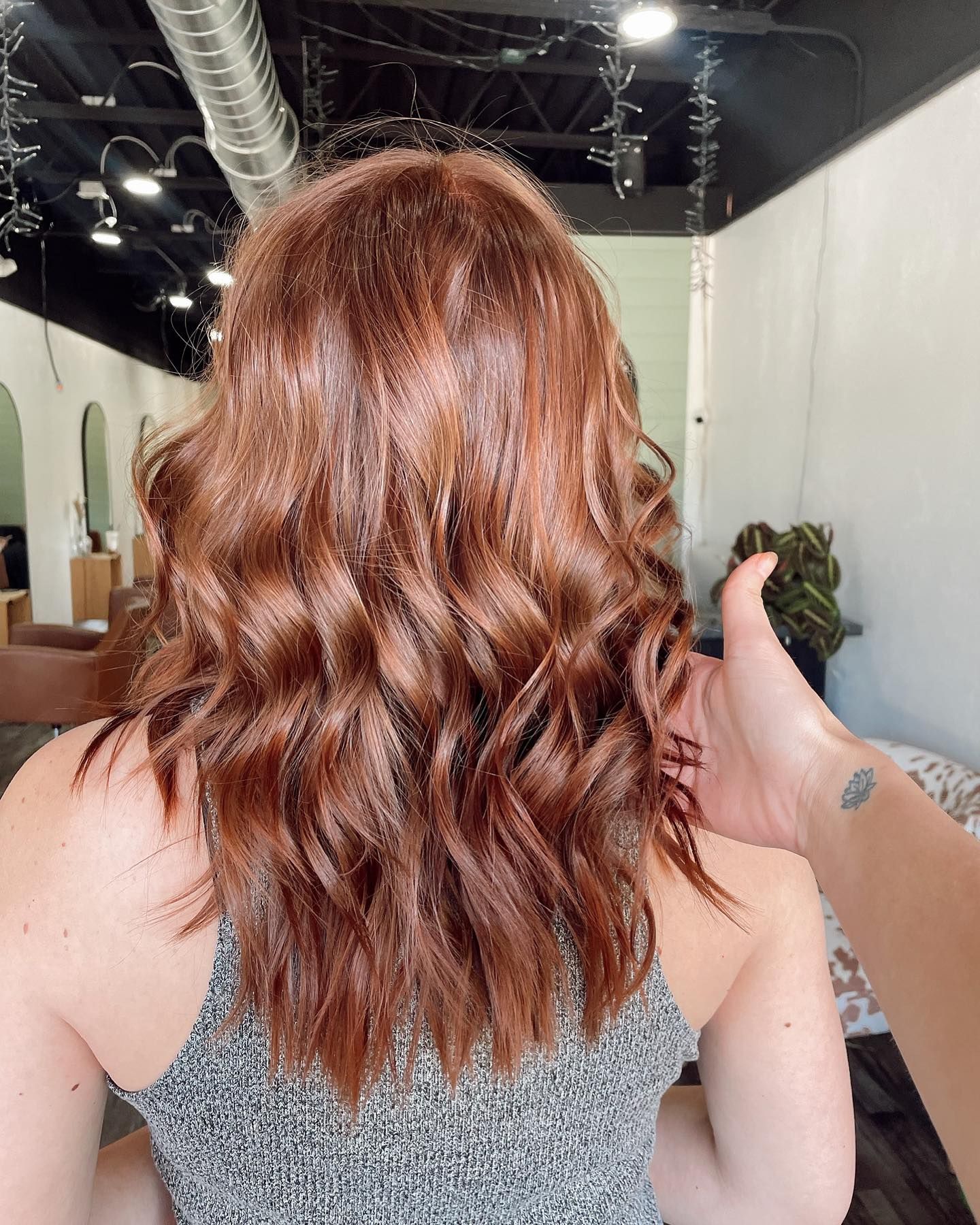 Woman with wavy, reddish-brown hair in a salon. A hand touches the hair.