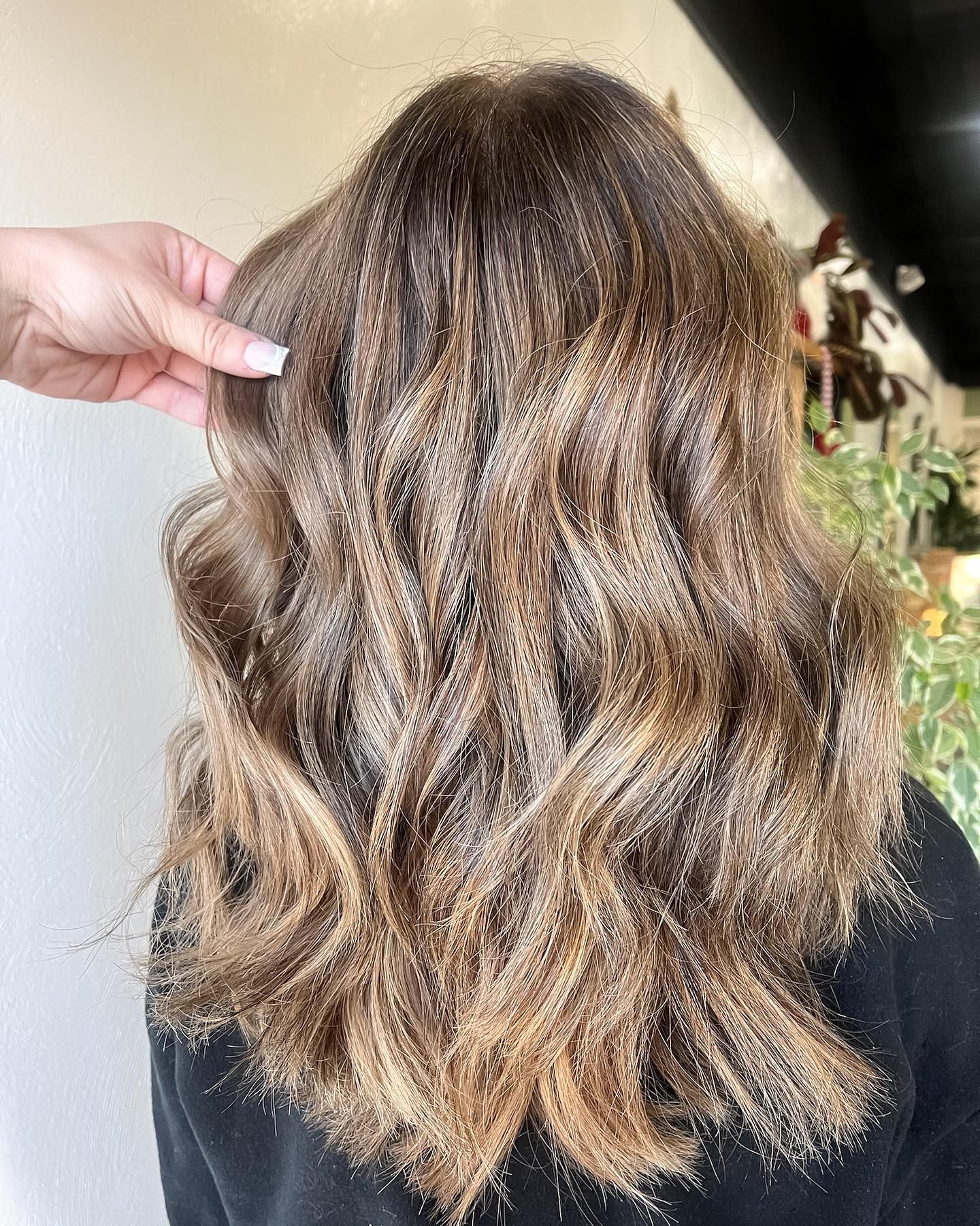 Brown wavy hair with highlights, being styled by a hand with manicured nails.
