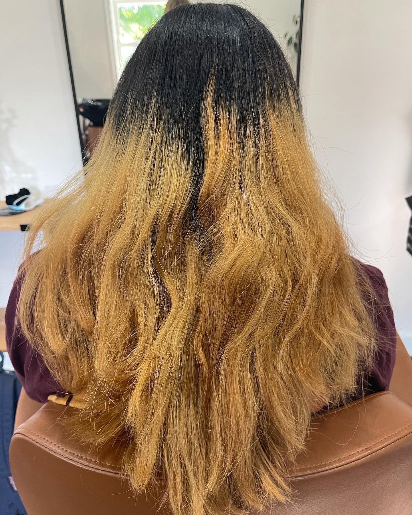 Black roots transitioning to blonde, wavy hair. The person is seated in a chair, hair in a salon.