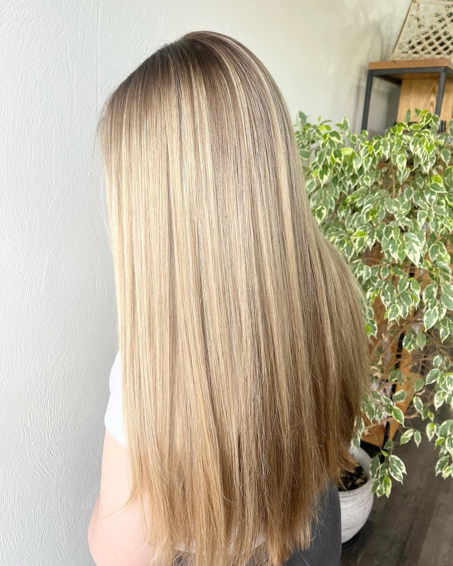 Woman with long, crimped blonde hair, with a gradient to darker ends. Leaning against a white wall.