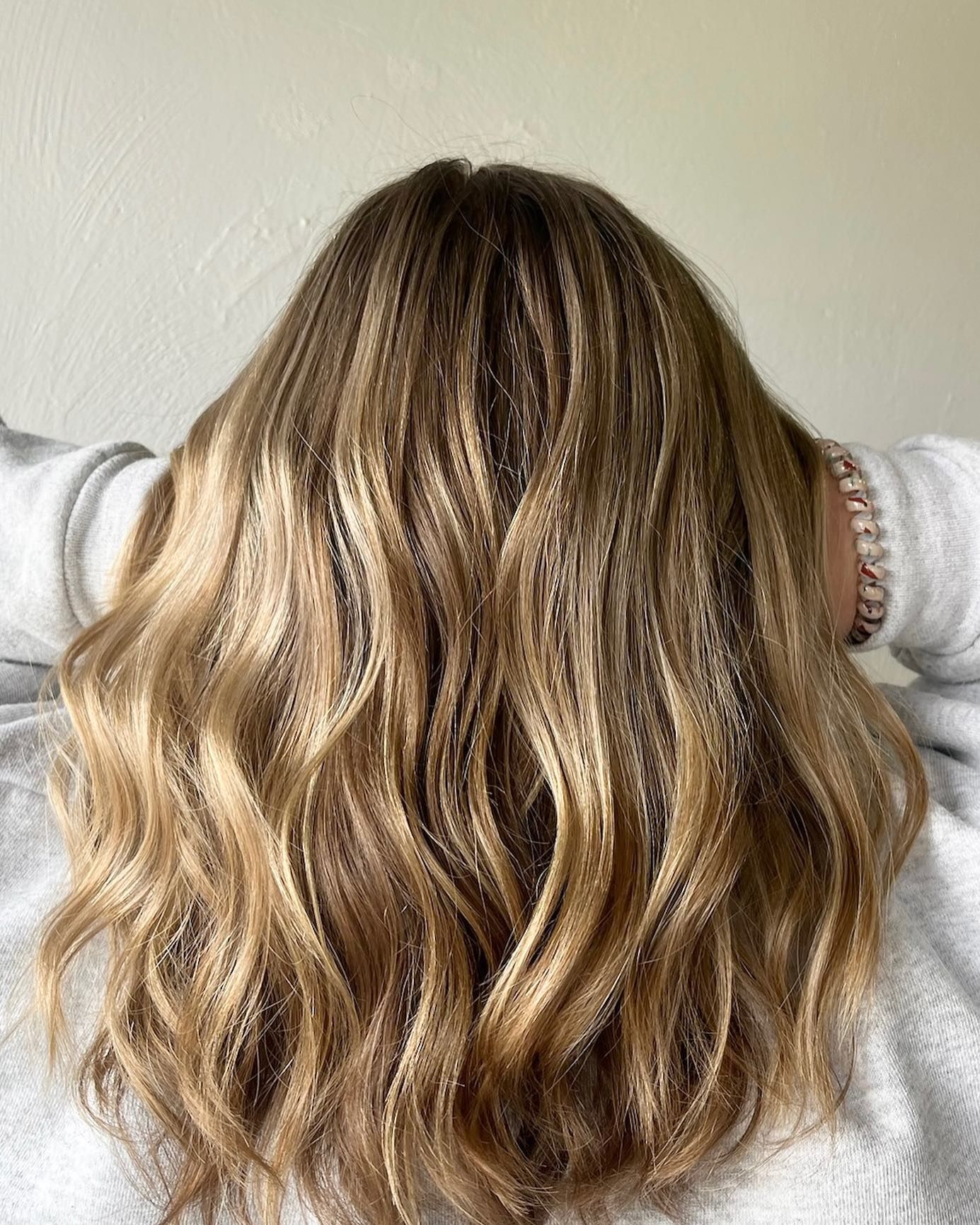Woman's long, wavy, light brown hair. Hands are resting behind the head.