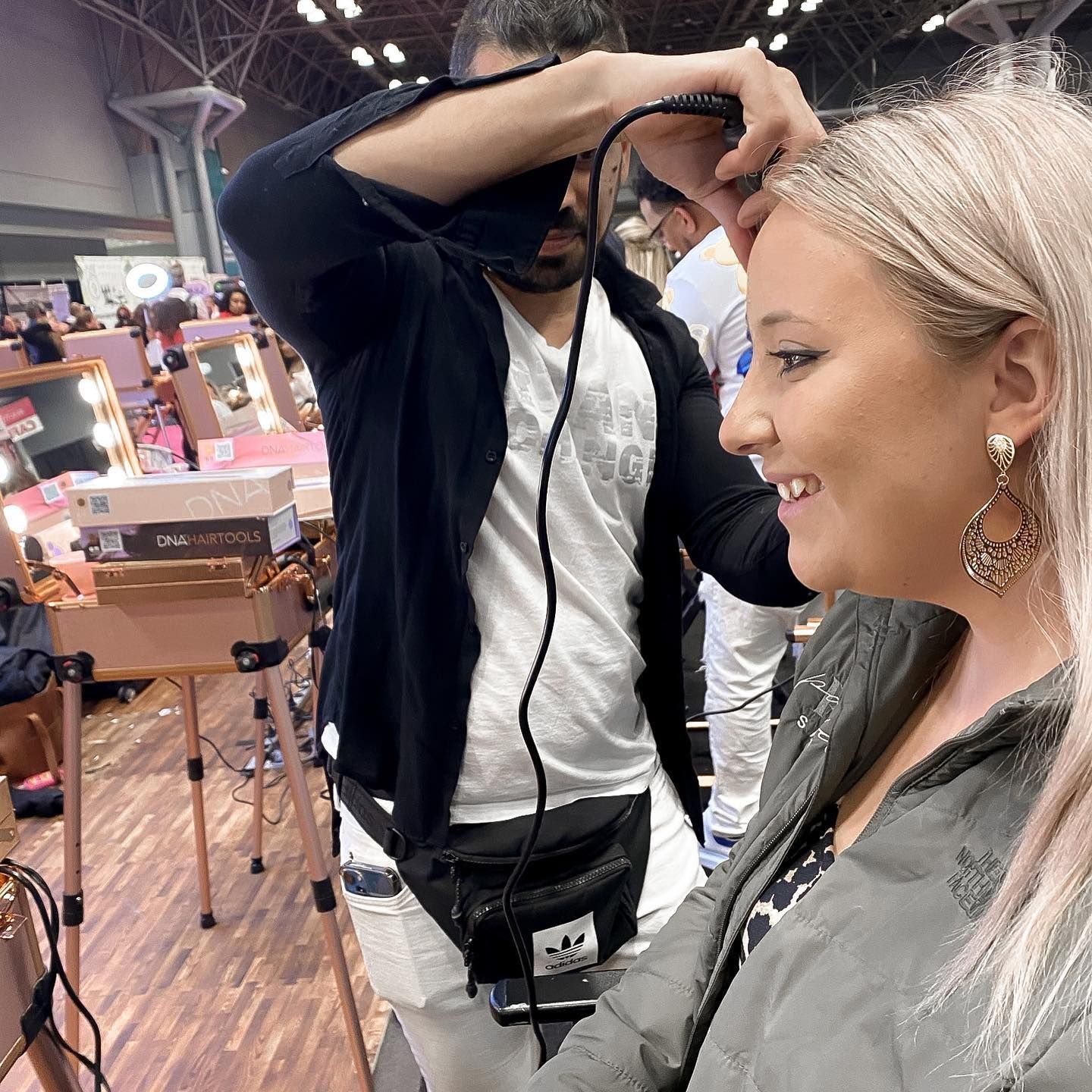 Man styling a woman's hair at a beauty event. Woman smiles as stylist uses curling iron.