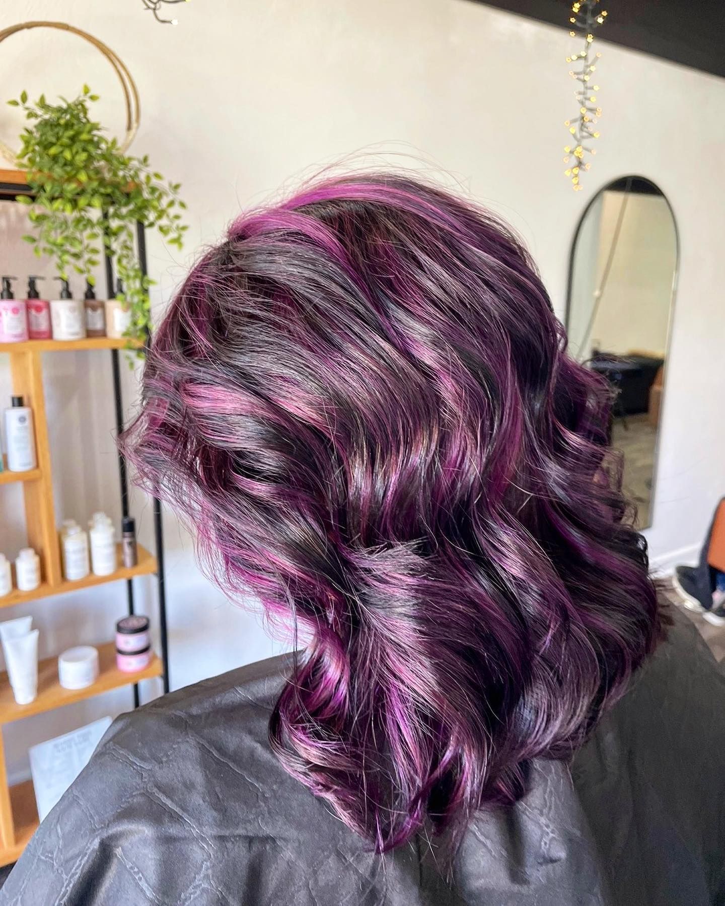 Woman's hair dyed dark with bright purple highlights, styled in loose waves. Salon setting.