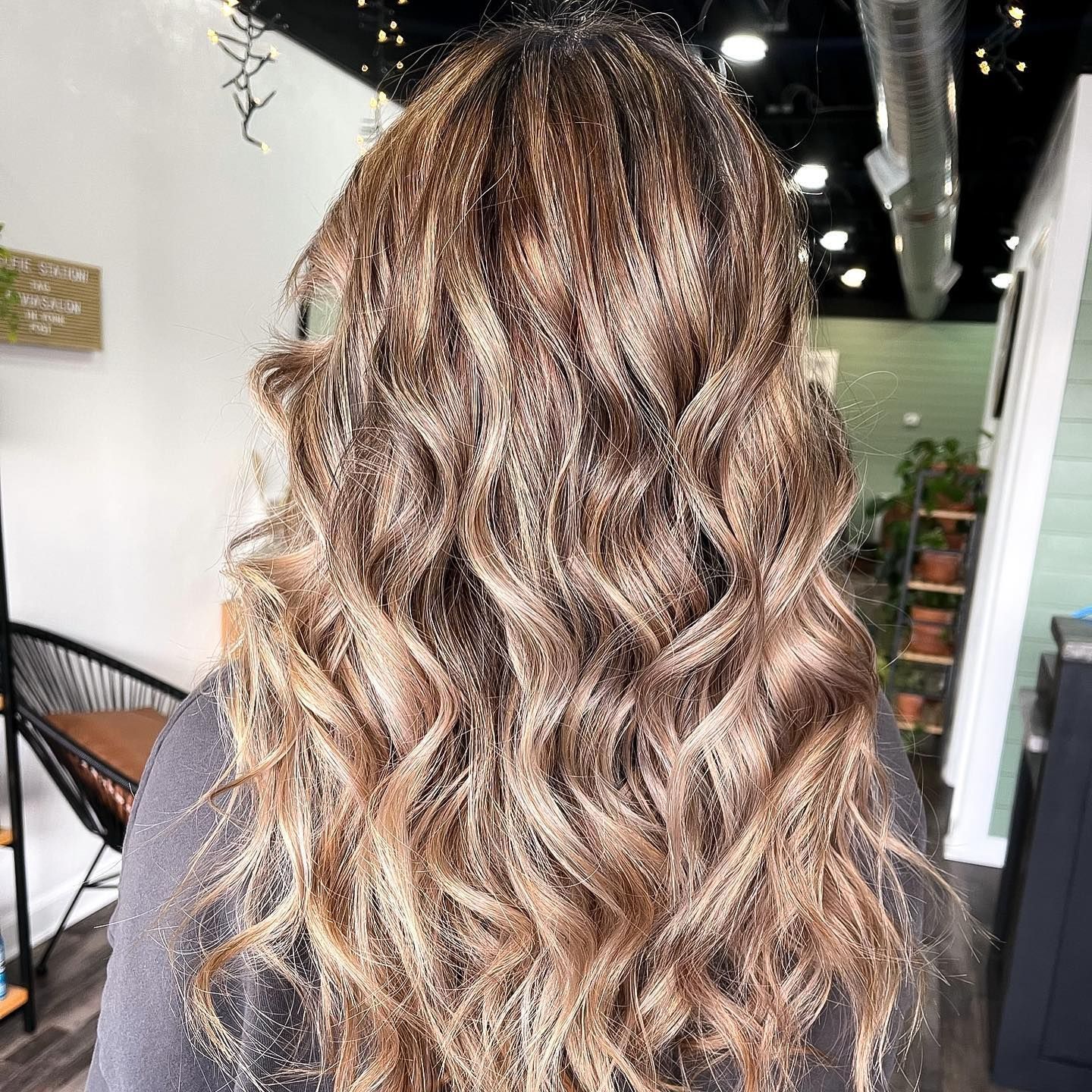 Woman with wavy, highlighted brown hair in a salon setting.