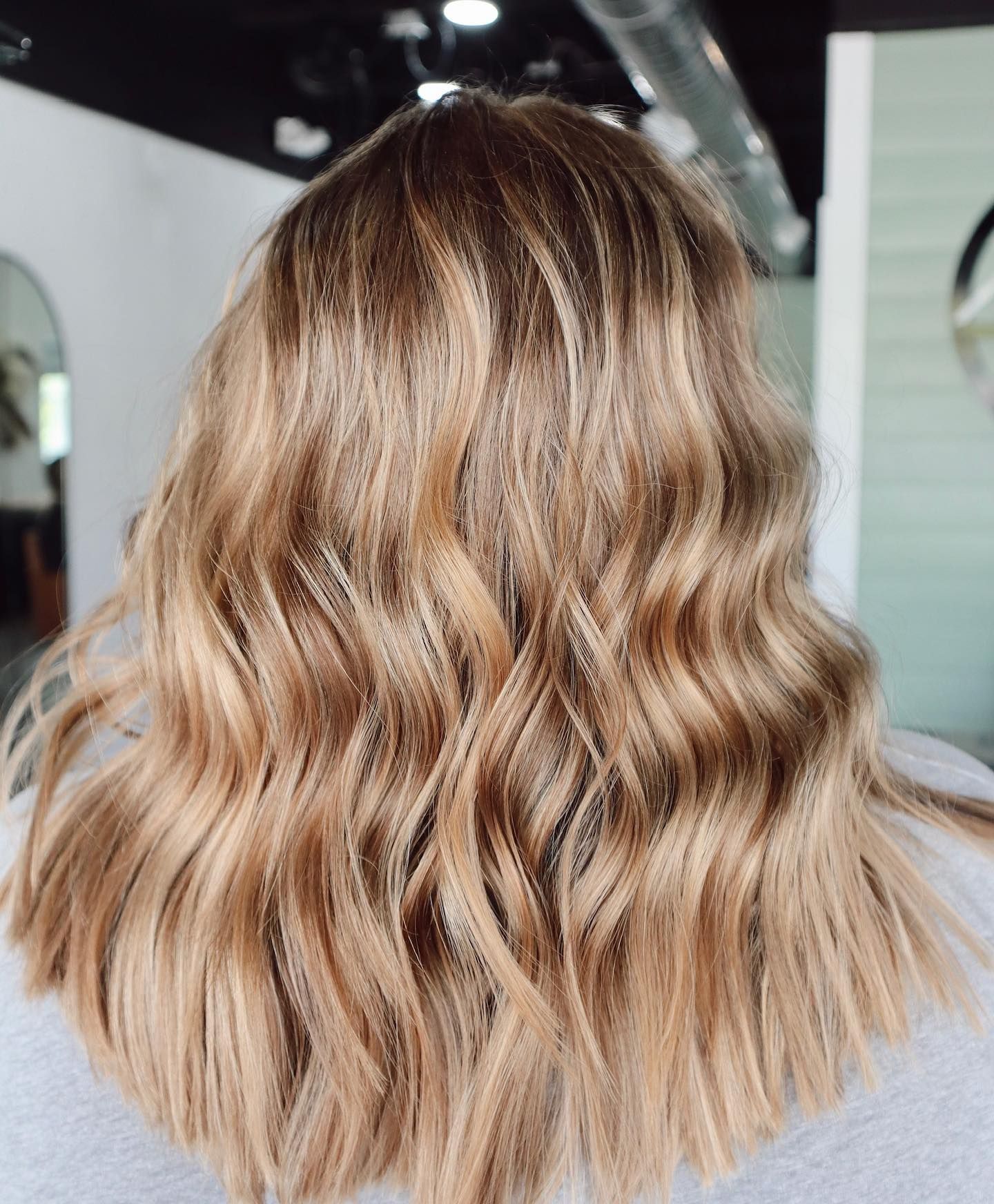 Wavy blonde hair styled with highlights, viewed from the back in a salon setting.