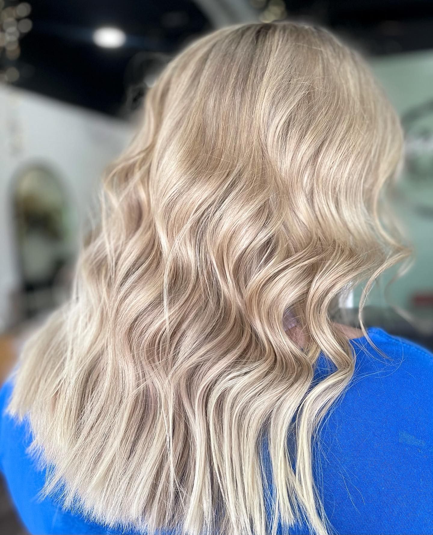 Blonde hair with loose waves; woman in blue sweater; salon setting.